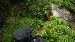 Geocacher mit uvex Regenjacke und Schutzausrüstung im abschüssigen und nassen Waldgelände