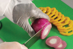 Person mit uvex HexArmor Schnittschutzhandschuhen unter lebensmittelechten Einweghandschuhen beim Zwiebelschneiden