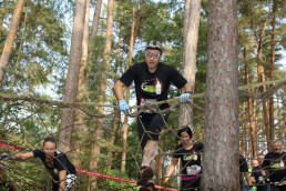 Teilnehmer am Runterra Geländelauf klettern mit uvex Schutzhandschuhen über ein zwischen Bäumen im Wald gespanntes Netz