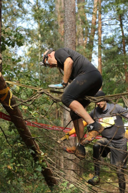 Dr. Wacker klettert mit seinen uvex Schutzhandshcuhen über ein im Wald gespanntes, grobmaschiges Netz.