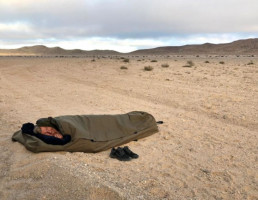 uvex Teilnehmer am Desert Dash ruht sich zwischen den Etappen in seinem Schlafsack mitten in der Wüste aus.