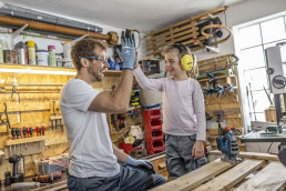 Vater und Tochter in uvex Schutzkleidung für die Freizeit geben einander in der Werkstatt ein High-Five.