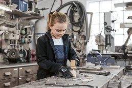 Mädchen in uvex Schutzkleidung beim Basteln mit Holz in der Werkstatt