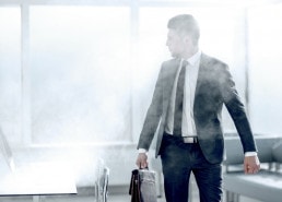 Mann mit Anzug und Aktentasche in einem Büro ist von Rauch umgeben.