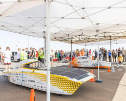 Das Covestro Photon Solarfahrzeug im Schatten, umringt von Rennteam-Mitgliedern und Zuschauern