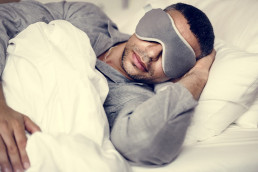 Mann mit Schlafmaske liegt schlafend im Bett.