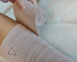 Person wickelt Bandagen um ein Bein.