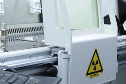 Labormitarbeiter ind Schutzkleidung vor einer Maschine, die radioaktive Strahlung einsetzt.