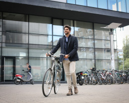 Mann schiebt sein Fahrrad über den Platz vor einem Bürogebäude.