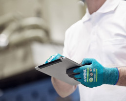 Mann bedient mit touchscreenfähigen uvex Bamboo TwinFlex Schutzhandschuhen ein Tablet.