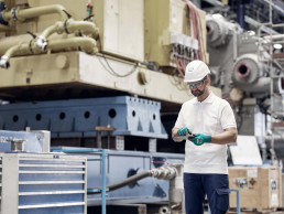 Arbeiter mit uvex Schutzhelm, Schutzbrille und Schutzhandschuhen vor Maschinen in einer Industriehalle.
