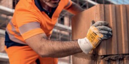 Bauarbeiter mit uvex Schutzhelm und Schutzhandschuhen setzt auf einer Baustelle Ziegel aufeinander.