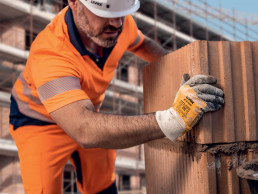 Bauarbeiter mit uvex Schutzhelm und Schutzhandschuhen setzt auf einer Baustelle Ziegel aufeinander.