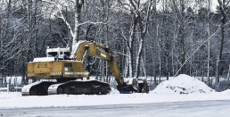 Ein Baustellen-Bagger im Schnee vor schneebedeckten Bäumen