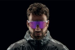 Mann mit reflektierender Jacke und lila getönten Sportsonnenbrillen vor schwarzem Hintergrund