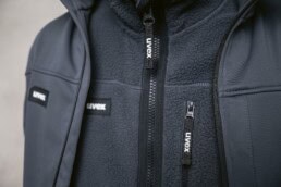 Detailaufnahme einer Arbeitsjacke mit UVEX-Logo und Reißverschluss.