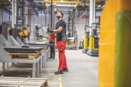 Ein Mann arbeitet in einer modernen Lagerhalle und bedient mit Handschuhen und Arbeitskleidung einen Hebeapparat