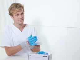 Ein Mann zieht sich uvex Einmalhandschuhe an