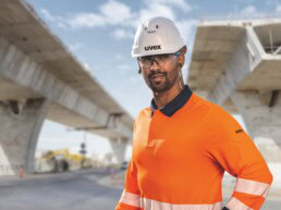 Ein Bauarbeiter mit Schutzhelm, Schutzbrille und Gehörschutz steht auf einer Brückenbaustelle